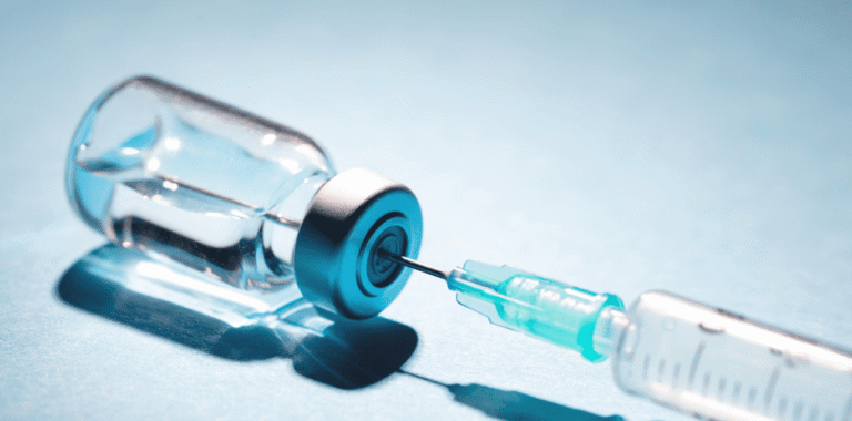 Syringe beside a clear vial on a blue background
