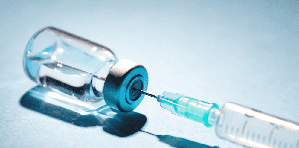 Syringe beside a clear vial on a blue background