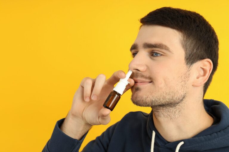 Man holding a nasal spray at his nose against a yellow background